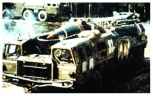 A Scud missile on its transport erector launcher (TEL), a large, camouflaged military truck, preparing for movement or launch in a field.